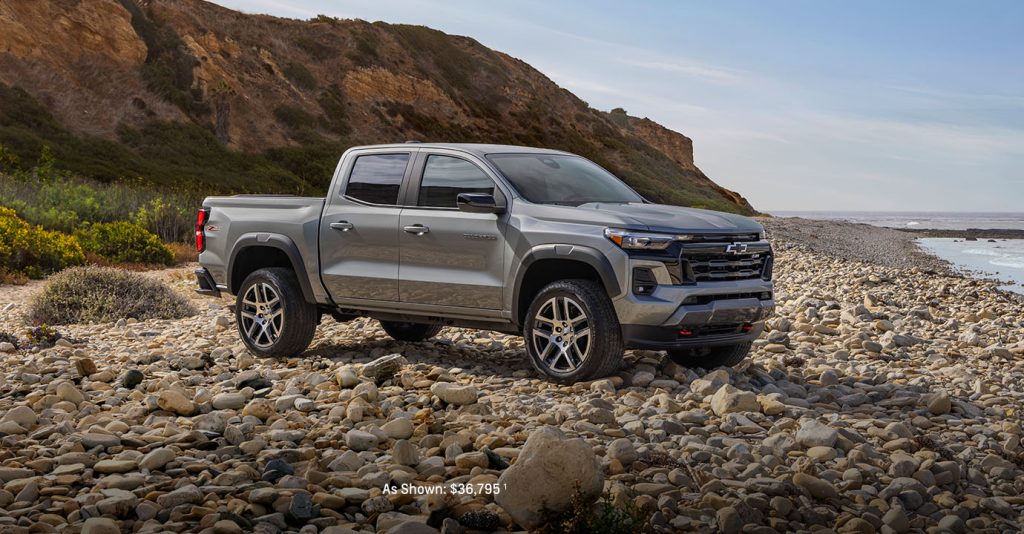2025 Chevrolet Colorado parked on a rocky beach with coastal cliffs in the background, showcasing its rugged design and off-road capability.