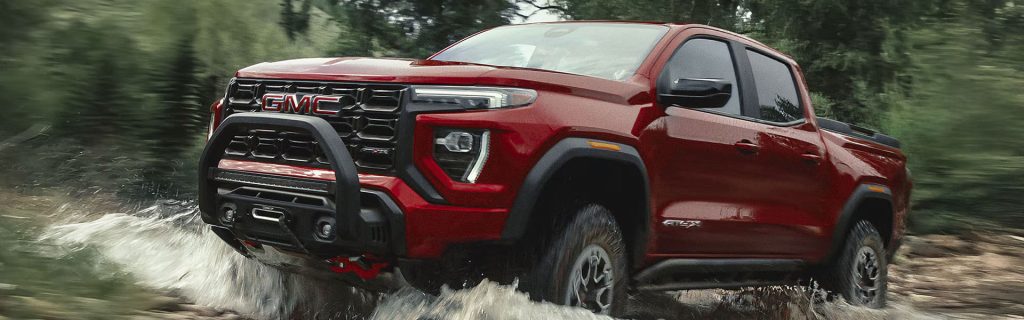 A red GMC truck driving through a muddy off-road terrain.