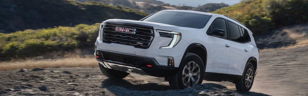 White 2026 GMC Acadia AT4 driving off-road on rocky terrain.