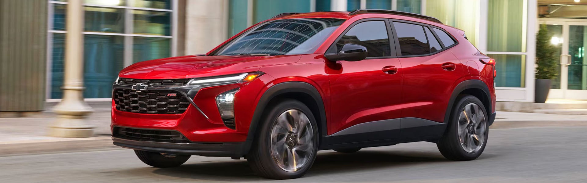 Red Chevrolet SUV driving through a city street with a modern building in the background.